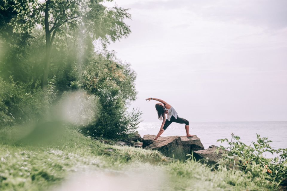 Person in athletic wear doing a standing side stretch outdoors on a rock by the sea