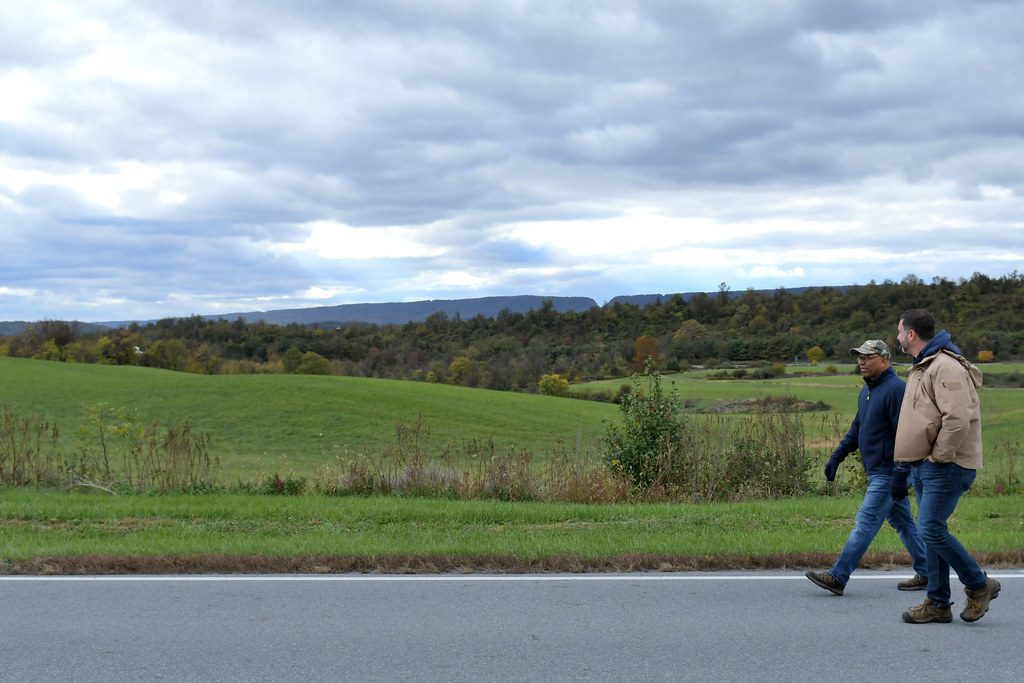Two people walking on a paved path beside an open grassy field under cloudy sky