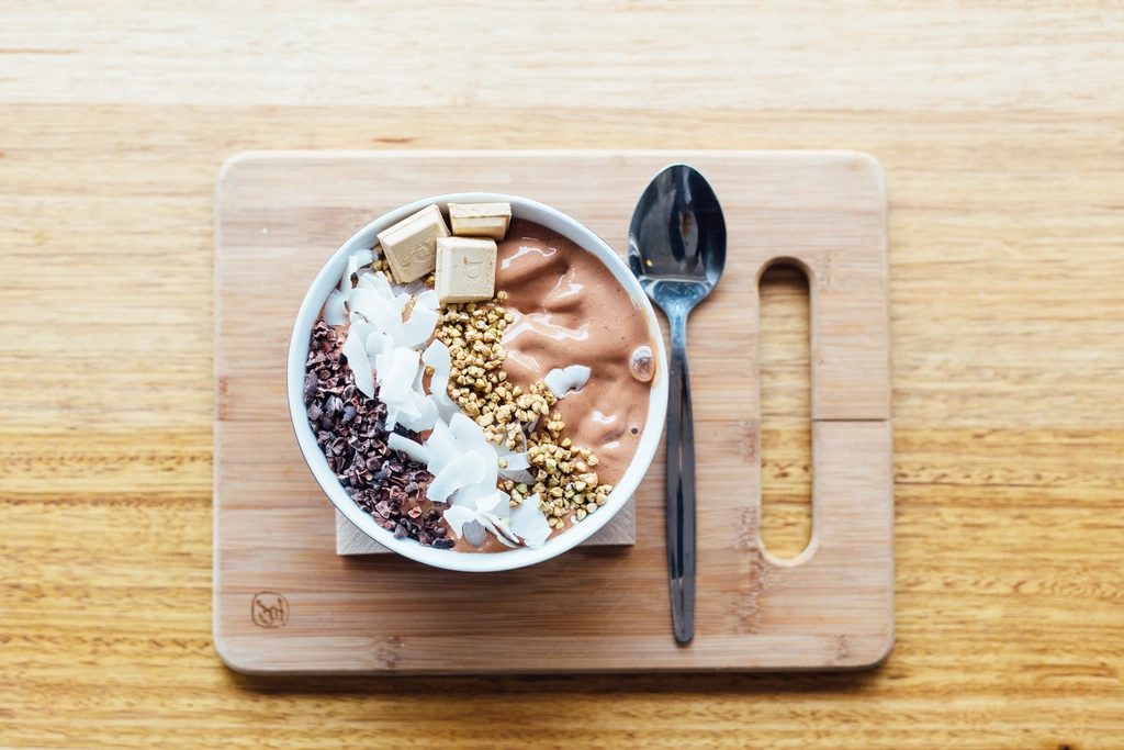 Overhead view of a smoothie bowl topped with granola and a spoon on a light wooden board