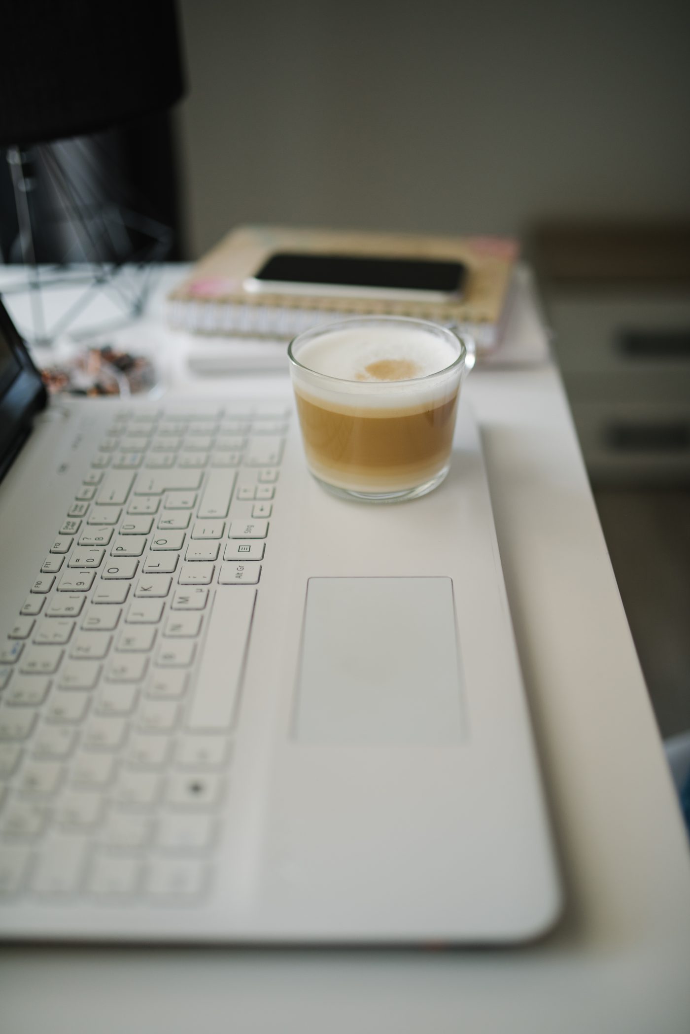 White laptop on a light desk with a cup of latte and a phone beside it
