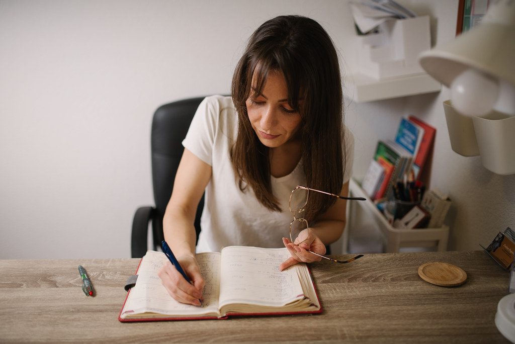 Woman at a wooden desk writing calmly in a notebook in natural light