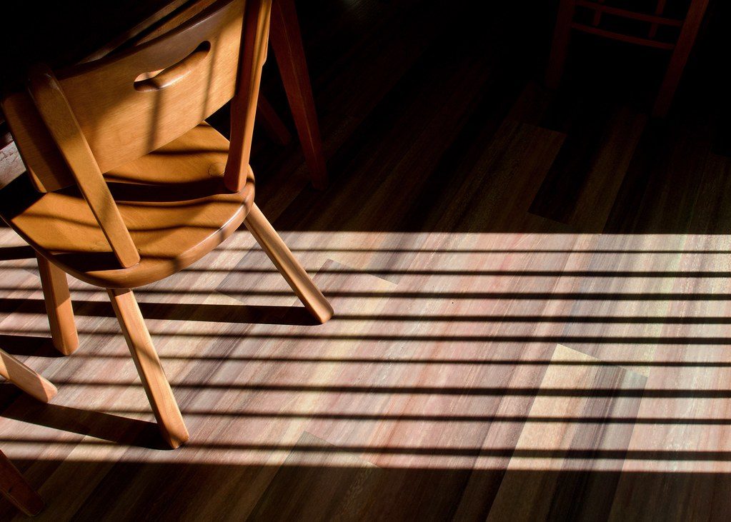 Wooden chair on a hardwood floor striped with warm sunlight coming through window blinds