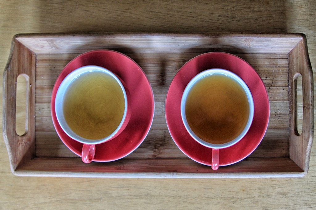 Two red saucers with white cups of tea on a wooden tray, seen from above